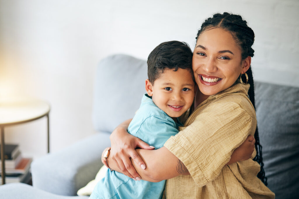 A young Latina mom hugs her son as they sit on a couch together.