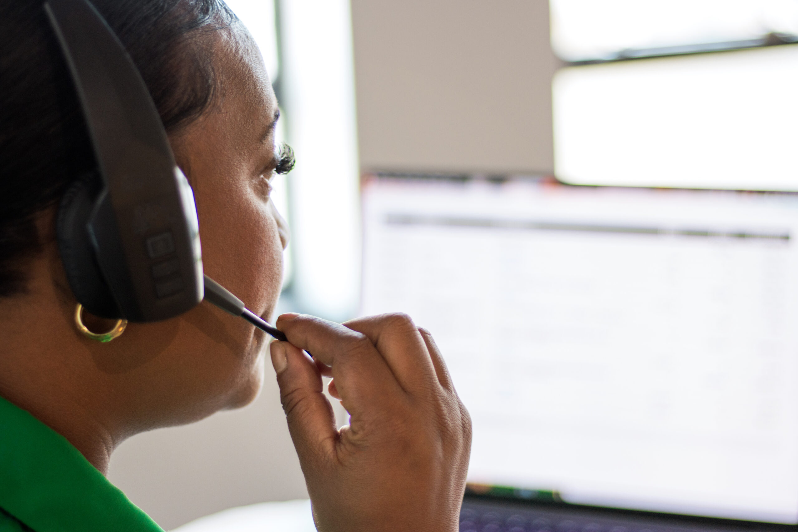A Black woman wearing a phone headset answers a call in a business setting.