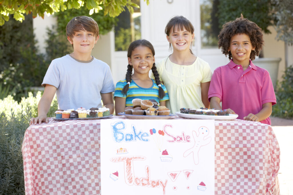 Children hosting a bake sale smile to the camera